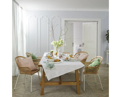 Table à manger décorée pour Pâques, entourée de chaises en rotin dans une pièce lumineuse.