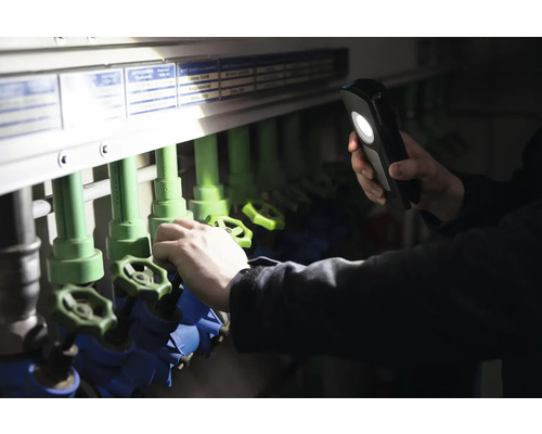 Une personne éclaire avec une lampe de poche un système de tuyauterie avec des vannes d''arrêt