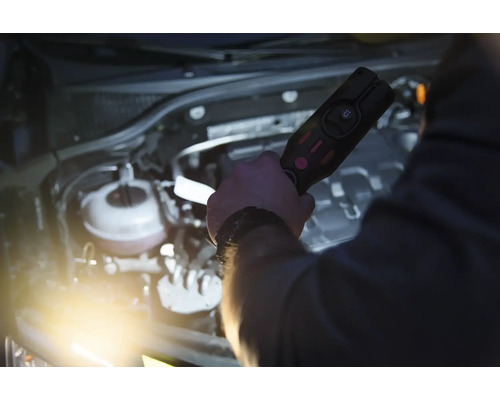 Une personne éclaire un compartiment moteur avec une lampe torche.