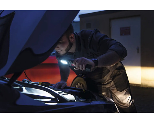 Un homme inspecte le compartiment moteur avec une lampe de poche