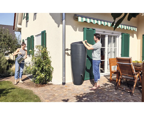 Personen nutzen eine Regentonne zur Gartenbewässerung in einem sonnigen Garten.