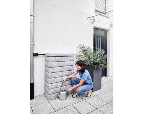 Frau befüllt Giesskanne an einem Regenwassertank im Garten.