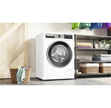 Machine à laver blanche de Bosch dans une pièce lumineuse avec panier à linge et étagère.