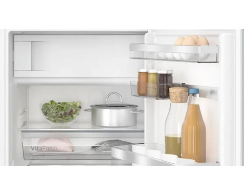 Innenansicht eines Kühlschranks mit Lebensmitteln wie Eiern, Salat, Fleisch, Fisch, Getränken und einem Kochtopf.