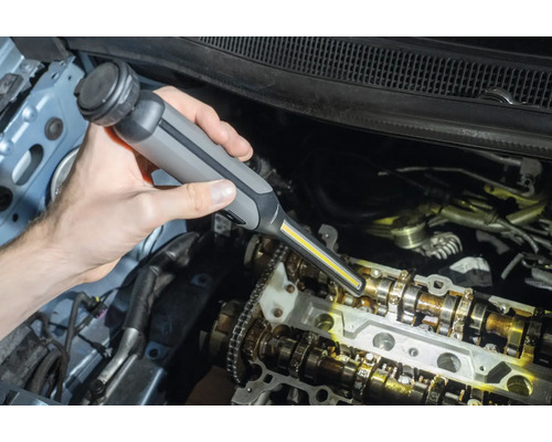 Une personne utilise une lampe d''atelier pour inspecter un moteur de voiture.