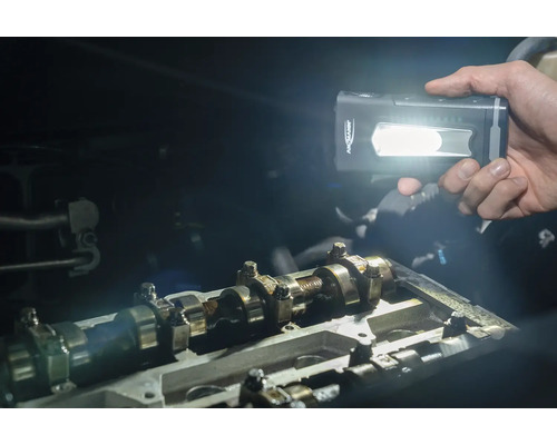 Une personne éclaire avec une lampe torche à batterie Ansmann dans un compartiment moteur ouvert.