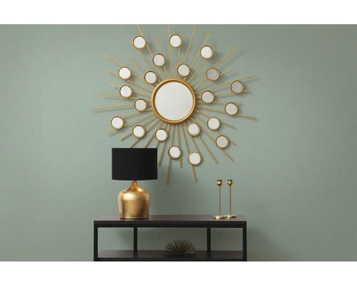 Arrangement décoratif avec miroir en forme de soleil, lampe de table et chandeliers sur une console.