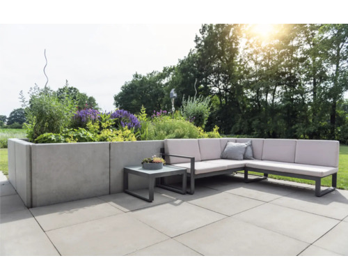 Terrasse avec salon de jardin en L, table d''appoint et plate-bande surélevée plantée.