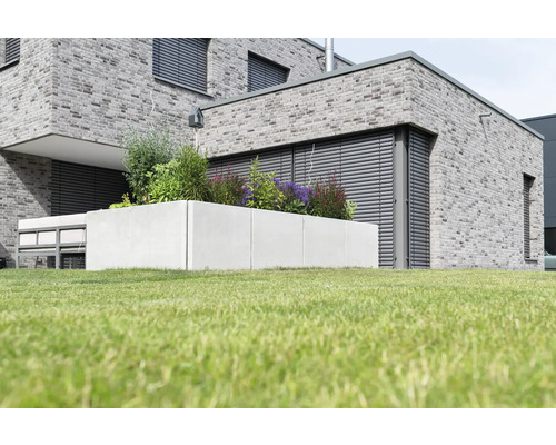 Jardinière en béton avec diverses plantes sur une pelouse devant une maison