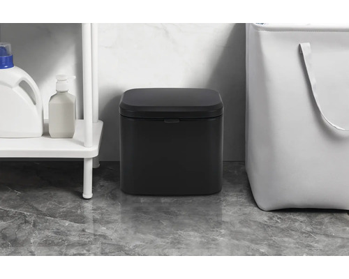 Schwarzer Treteimer im Badezimmer neben einem Regal und einem Wäschekorb.