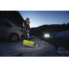 Frau schippt Schnee mit einer Schneeschaufel vor einem Auto.