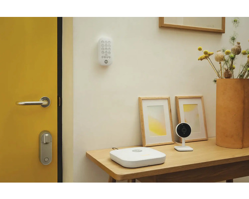 Scène avec des composants de système de sécurité Yale, comprenant un clavier, une station de base et une caméra sur une table