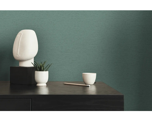 Dekorative Szene mit Skulptur, Pflanze, Tasse und Bleistift auf einem Tisch vor einer strukturierten Tapete