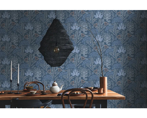 Une salle à manger avec une table en bois, de la vaisselle, une suspension et un papier peint à motifs floraux.