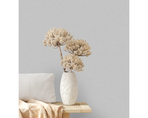 Dekorative Vase mit Trockenblumen auf einem Tisch mit Kissen vor einer strukturierten Wand