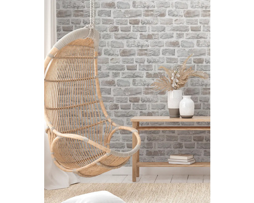 Fauteuil suspendu en rotin dans une pièce lumineuse et agréable avec du papier peint imitation briques