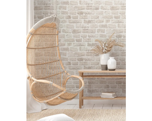 Szene mit einem hängenden Korbsessel, einem Holztisch und Dekorationsgegenständen vor einer Ziegelwand.