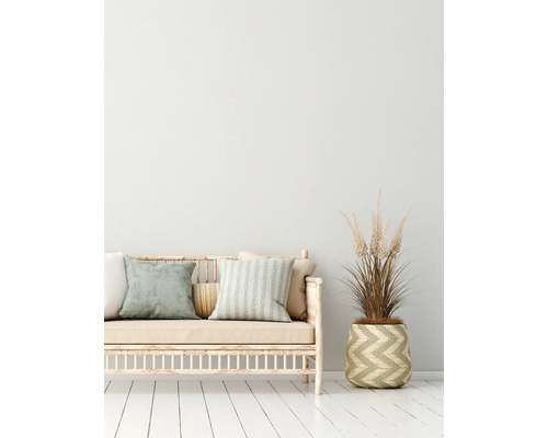Dekoratives Sofa mit Kissen und einer Pflanze in einem Korb auf einem weißen Holzboden.