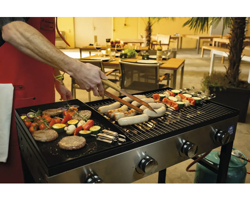 Une personne fait griller des saucisses, des brochettes de légumes et des hamburgers sur un gril à gaz à l''extérieur.