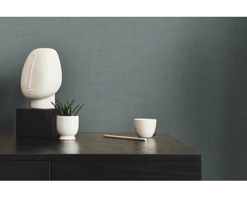 Dekorative Szene mit Skulptur, Pflanze und Tasse auf einer dunklen Holzkommode vor einer einfarbigen Wand.