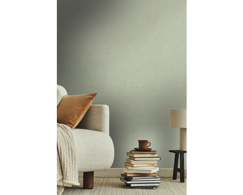 Salon avec papier peint textile, canapé, coussin, couverture, pile de livres, tasse et lampe sur un tabouret