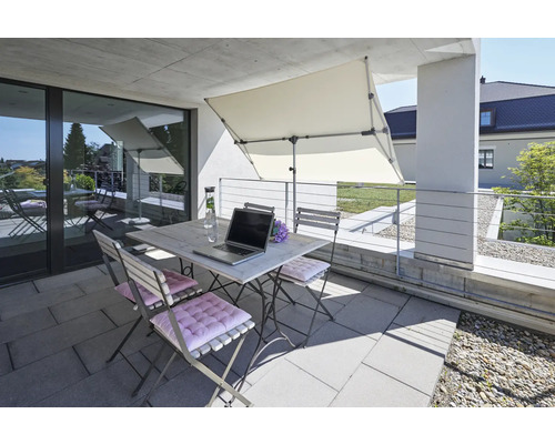 Balcon avec table pliante, chaises pliantes, parasol, ordinateur portable et bouteille de boisson