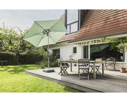 Scène de jardin avec un parasol carré, une table et des chaises sur une terrasse en bois devant une maison.