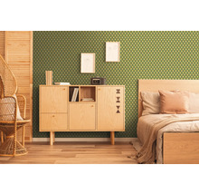 Chambre avec papier peint vert à motif géométrique, armoire en bois, lit et chaise en rotin.