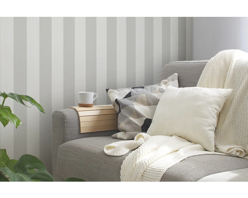 Wohnzimmer mit gestreifter Tapete, Sofa mit Kissen und Decke sowie einem Tablett mit Tasse.