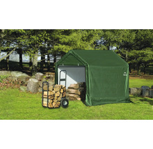 Grünes Gerätehaus mit Brennholz und Wagen im Garten.