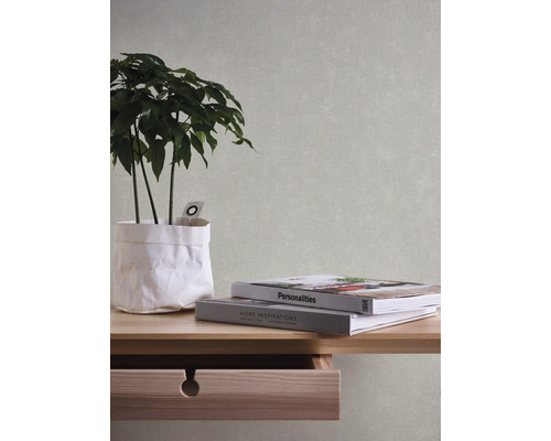 Nahaufnahme einer Wand mit einer hellen Vliestapete in Textiloptik sowie einem Tisch mit Pflanze und Büchern