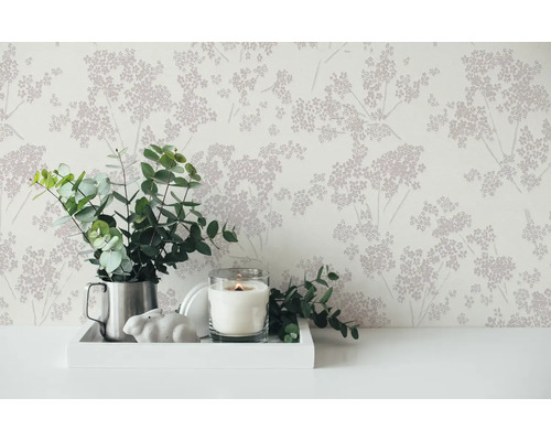 Arrangement décoratif avec papier peint floral, eucalyptus dans un pichet, bougie et figurine de lapin sur un plateau.