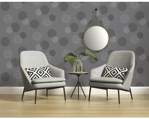 Deux fauteuils et une table avec une plante devant un mur avec du papier peint à motifs à pois et un miroir.