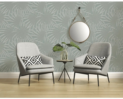 Raumansicht mit zwei grauen Sesseln, kleinem Tisch mit Pflanze, rundem Spiegel und Tapete mit Palmenmuster