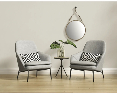 Zwei graue Sessel mit Kissen, ein runder Spiegel und ein Beistelltisch mit einer Pflanze in einem hellen Raum.