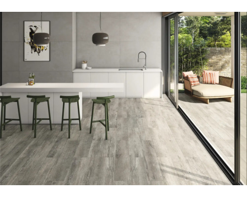 Pièce lumineuse avec carrelage imitation bois, kitchenette et accès à une terrasse avec des sièges.