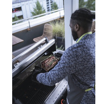 Mann bereitet Braten auf Grill im Freien zu