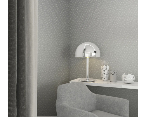 Scène avec un papier peint à losanges gris, une lampe argentée, des articles de décoration et un fauteuil gris