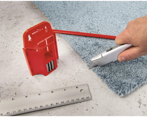 Cutter coupant de la moquette à côté d''un coupe-moquette et d''une règle