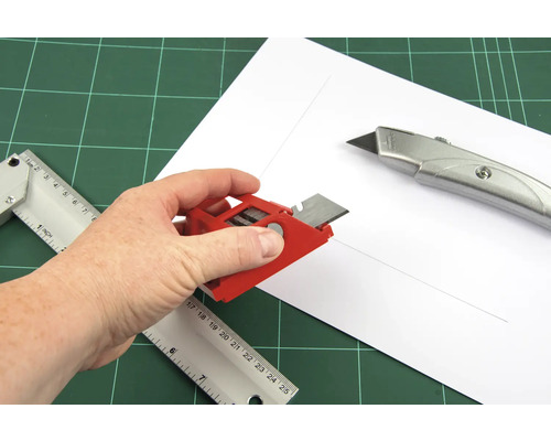 Main avec outil de coupe, règle et cutter sur tapis de découpe