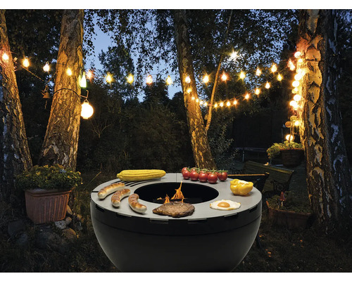 Grillszene im Garten mit Grill, Grillgut und Lichterkette.