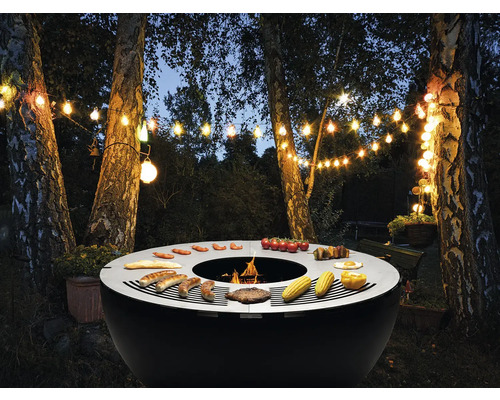 Kugelgrill im Garten mit Grillgut unter Lichterkette