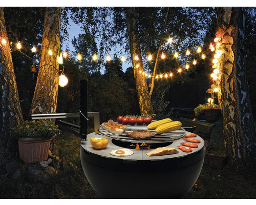 Kugelgrill mit Grillgut und Lichterkette im Garten