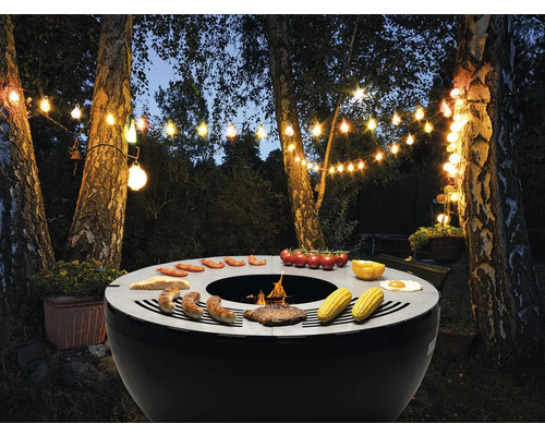 Gartenszene mit beleuchteter Grillstelle und zubereiteten Speisen wie Wurst, Gemüse und Brot