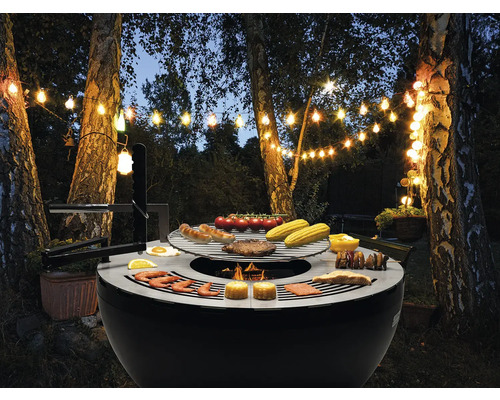 Abendliche Gartenszene mit Grill, beleuchtet mit Lichterketten, mit Speisen wie Würstchen und Gemüse.