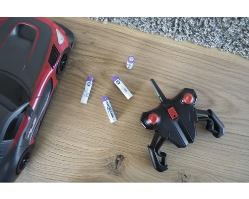 Voiture jouet, télécommande et piles sur un plancher en bois