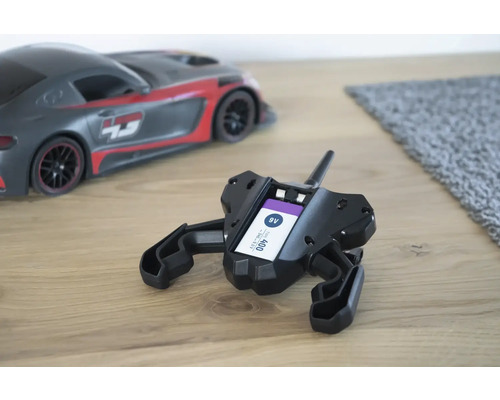 Télécommande noire avec pile 9V insérée et voiture jouet en arrière-plan