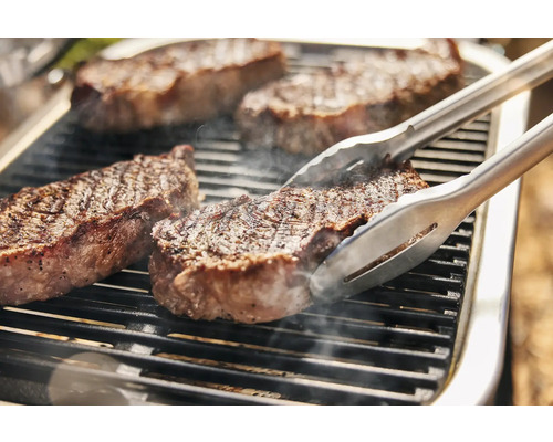 Des steaks sont grillés sur un barbecue à l''aide d''une pince à barbecue.