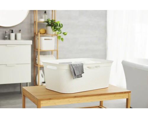 Panier à linge clair en plastique sur une table en bois dans une salle de bain.