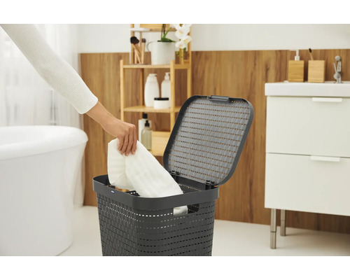 Scène de salle de bain avec un panier à linge avec couvercle dans lequel une personne dépose une serviette blanche.